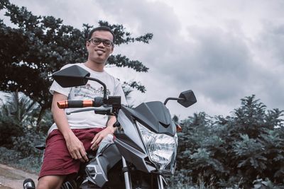 Low angle portrait of man riding motorcycle against cloudy sky