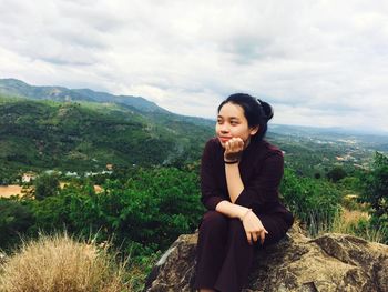 Young woman sitting on landscape against sky