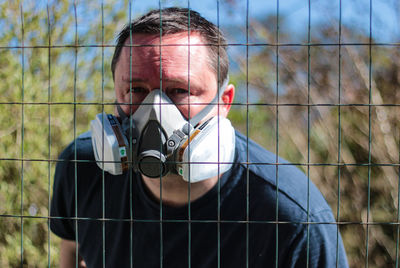 Portrait of man wearing mask seen through fence