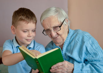 Portrait of white-hair eldery woman 90 years old with her grandson at home, reading book together