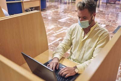 A boy wearing a mask is studying in a personal cabin in the library