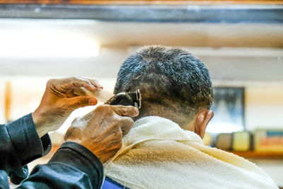 Cropped hands of barber cutting male customer hair in shop