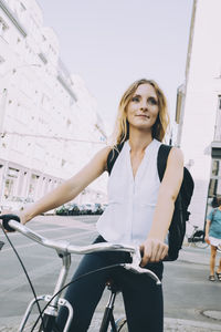 Smiling businesswoman riding bicycle on road in city against sky