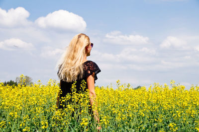 Rear view of young woman standing on oilseed rape field