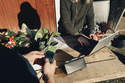 Customer paying with credit card while farmer using laptop at market