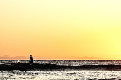 Silhouette man in sea against orange sky