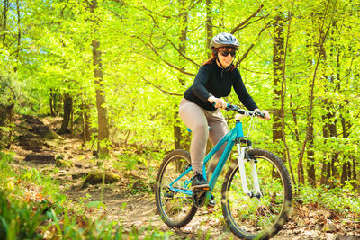 Full length of smiling woman riding bicycle in forest