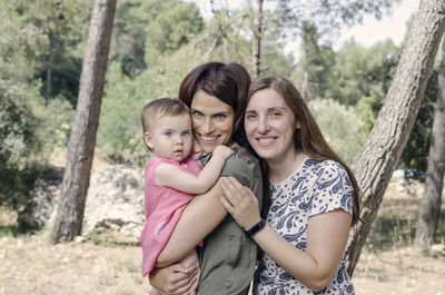 Portrait of happy mother with daughter standing against trees