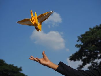 Low angle view of hand throwing origami against sky