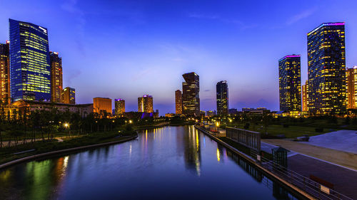 River by illuminated buildings against sky at dusk