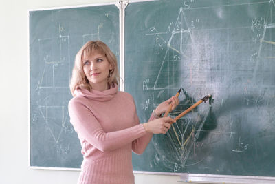 Confident teacher explaining diagram on blackboard in classroom