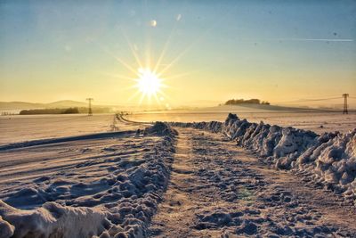 Snow covered landscape against sky during sunset