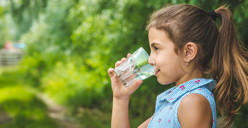 Side view of girl drinking water from glass while looking away