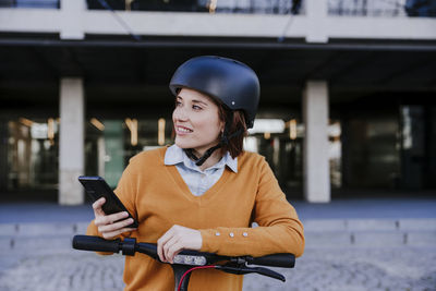 Happy woman standing with smart phone near building