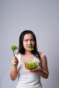 Portrait of young woman holding ice cream against gray background