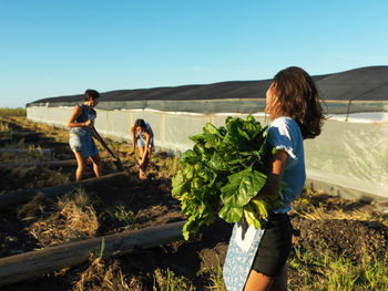 Woman with friends holding leaf vegetables at farm
