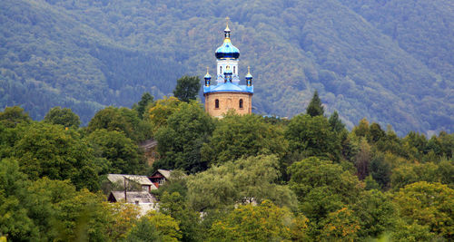 Church amidst trees and buildings against mountain