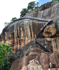 Low angle view of people on rock formation against sky