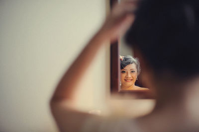 Smiling bride looking at mirror against wall