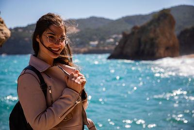 Portrait of smiling young woman standing against sea