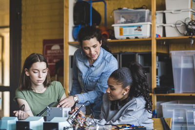 Female teacher assisting high school teenage students preparing robot on desk in classroom