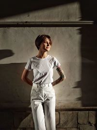 Young woman looking away while standing against wall