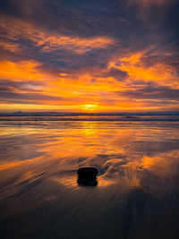 Rock on wet sand at low tide with beautiful dramatic sunset in encinitas, california