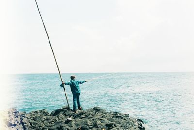 Man fishing in sea against clear sky