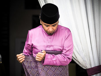 Man holding umbrella standing against pink wall