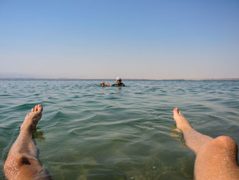 Low section of people on beach against clear sky