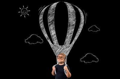 Digital composite image of boy flying hot air balloon against black background