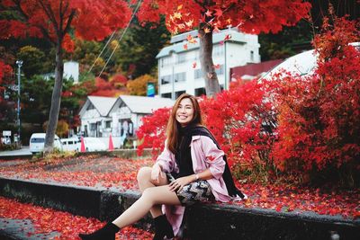 Full length portrait of woman sitting on red autumn leaves