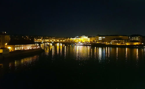 Illuminated buildings by river against sky at night