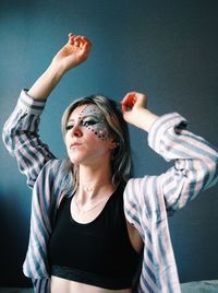 Young woman with face paint and arms raised looking away at home