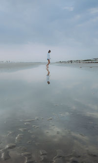 Rear view of woman standing on beach against sky