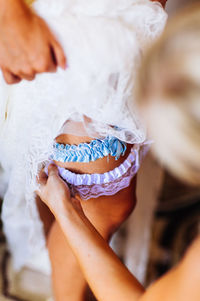 Cropped hands of woman dressing up bride at home