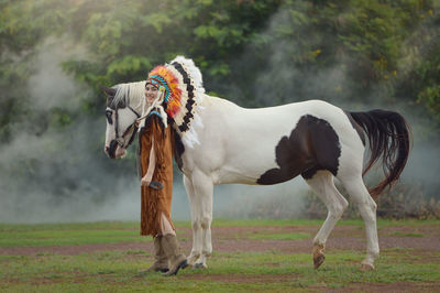 Young woman wearing traditional clothing standing with horse on land
