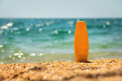 Empty cosmetic skin care cream or sunscreen on sandy beach on sea background. a yellow bottle of
