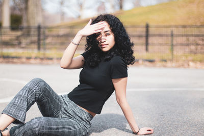 Portrait of woman shielding eyes while sitting on road