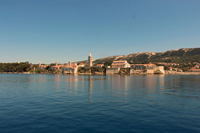 Buildings by sea against clear blue sky