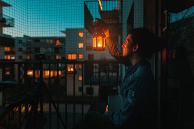 Side view of woman holding oil lamp while sitting in balcony at dusk