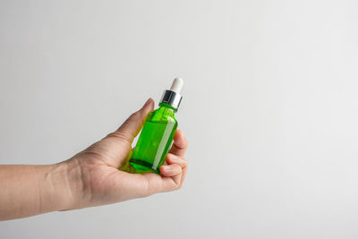 Close-up of hand holding bottle against white background