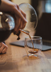 Cropped hand pouring coffee in drinking glass on wooden table