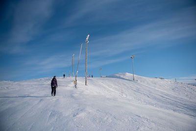 Rear view of person walking on snow covered field against sky
