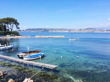Boats moored in sea against blue sky