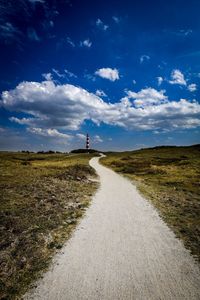 Dirt road amidst field against sky