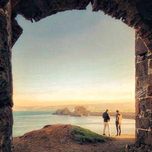 Rear view of men standing at beach during sunset