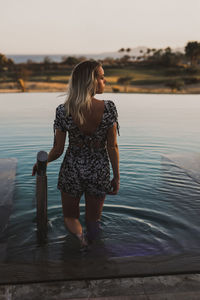 Rear view of woman standing in lake against sky