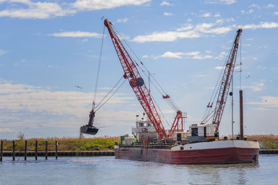 Cranes at commercial dock against sky