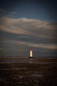 Lighthouse by sea against sky during sunset